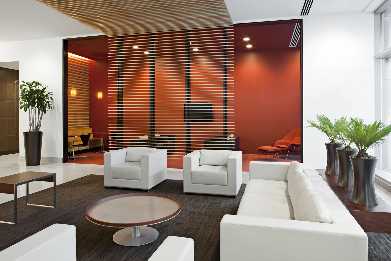 A lounge with white sofas and a glass-walled meeting room
