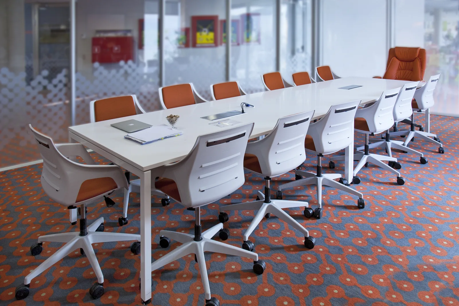 A meeting room with a long white table and orange chairs